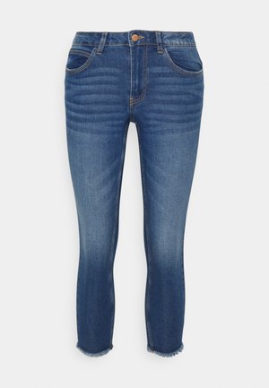 Jeans de ganga azuis com corte slim, apresentando uma cintura de altura média, cinco bolsos e barras desfiadas. Fading sutil e detalhes de costura presentes.