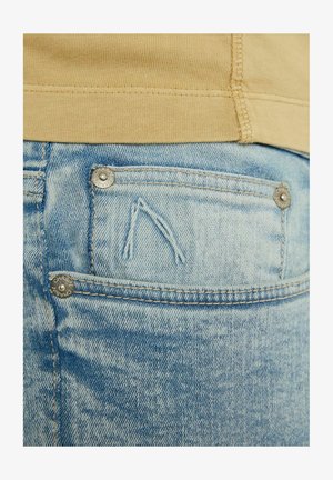 I jeans in denim blu chiaro presentano una tasca consumata con cuciture visibili e dettagli in metallo. Il tessuto ha una texture liscia e usurata.