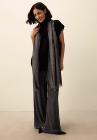 Haut noir à manches courtes, large pantalon gris à motifs, et écharpe texturée grise, assortis à des chaussures noires à bout pointu.