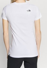 Bílá bavlněná tričko s krátkým rukávem. Obsahuje malé černé logo "The North Face" na horní části zad. Jednoduchý a lehký design.