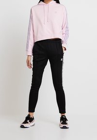 Rosa kort hoodie med vit logotyp, kombinerad med svarta slim-fit byxor med vita sidostråk. Bärs med svarta och rosa sneakers.