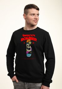 Svart sweatshirt med en färgglad grafisk design av ett dödskalle med graffiti-inslag, fet röd text "STREET BOMBER" och ribbad mudd.