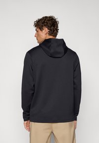 Black hoodie with a textured fabric, featuring a drawstring hood, long sleeves, and a relaxed fit. Simple design without logos or patterns.