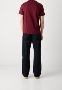 Vínová bavlněná tričko s krátkým rukávem v kombinaci s volnými tmavě modrými riflovými kalhotami. Boty jsou světlé barvy s hladkým povrchem.