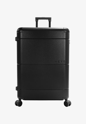 Valise rigide noire à quatre roues avec poignée télescopique, marquée "Heys" au centre avant.