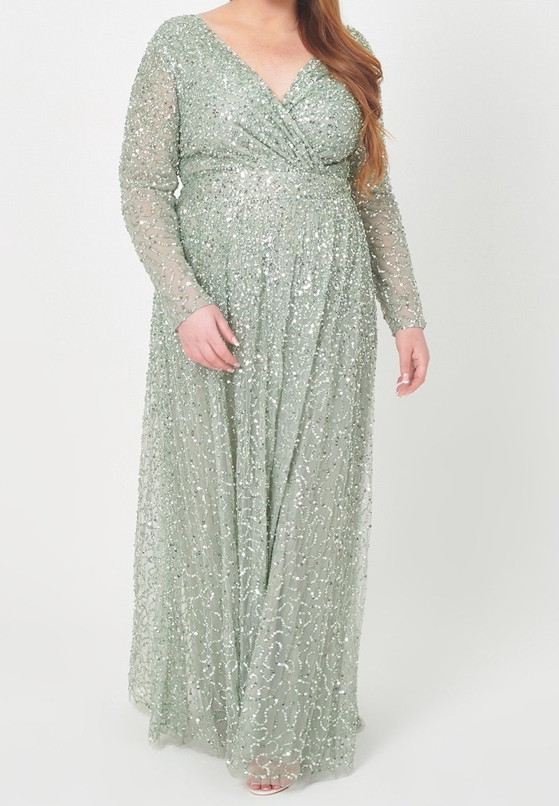 Femme porte une robe longue vert pâle à manches longues, au sol, avec des motifs en sequins et un corsage portefeuille en V.