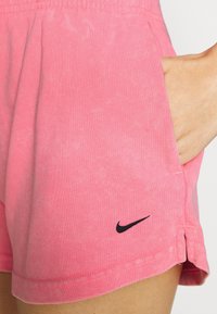 Rosa bomullsshorts med elastisk midja, fickor och en svart Nike-logotyp på sidan. Tyget har en subtil textur.