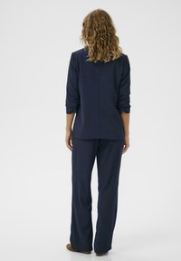 Tengerészkék loungewear szett, amely hosszú ujjú felsőből áll, felgöngyölt ujjakkal és laza szabású nadrággal, puha anyagból, sima textúrával.