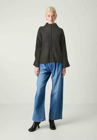 Tamsus, raukšlėtas megztinis su aukštu apykakle, derinamas su plačiomis mėlynomis džinsinėmis kelnėmis. Modelis vilki juodus aulinukus.