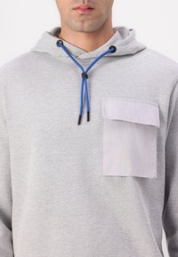 Gray hooded sweatshirt with blue drawstring and contrasting patch pocket. Material appears soft and textured, suitable for casual wear.