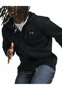 Haut à capuche zippé noir avec une texture lisse et un logo Under Armour gris sur la poitrine gauche. Comprend une capuche ajustable et des poches latérales.