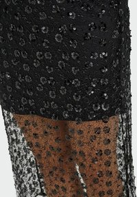 Melna mežģīņu kleita ar ziedu aplikācijām no spīdīgiem fliteriem, caurspīdīgu tekstūru un kārtainu dizainu ar plūstošu apakšu.