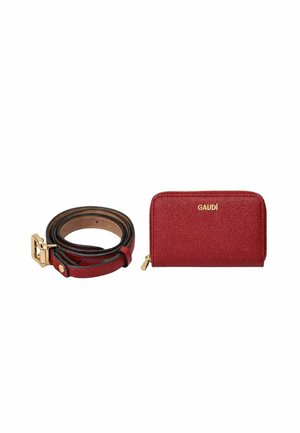 Cintura in pelle rossa con fibbia dorata accanto a un portafoglio rosso con cerniera, impresso con la scritta "GAUDÌ" in oro su sfondo bianco.