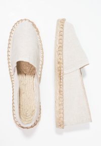 Beige espadrilles with a textured fabric upper, jute rope midsole, and a soft, flexible design. Features stitched accents along the edges.