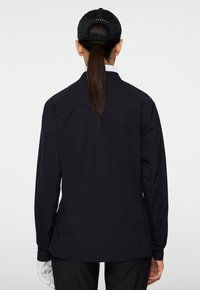 Svart långärmad skjorta med rak skärning, utrustad med krage och ribbade manschetter. Baksidan visar en slät yta utan synliga mönster.