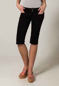 Pantalons capri noirs arrivant au genou avec une texture lisse, dotés de deux boutons à l'avant, de poches latérales et d'un design ajusté, accompagnés de sandales à plateforme roses.