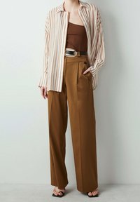 Striped long-sleeve shirt in white and brown, paired with high-waisted brown pants featuring a front pleat and a large black belt buckle.