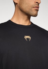 Sort kortærmet t-shirt med rund hals, prydet med et guld slange-logo på venstre bryst. Blødt stof med en glat tekstur.
