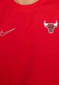 Camiseta deportiva roja con el logotipo blanco de Nike en el lado izquierdo y el logotipo de la cabeza de toro de los Chicago Bulls en el lado derecho del pecho.