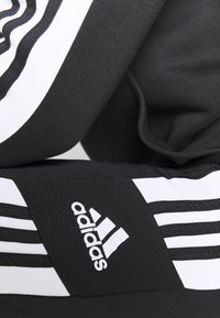 Schwarze Sporthose mit weißen Streifen und Adidas-Logo; glatte Textur mit enganliegendem Design und elastischem Bund.