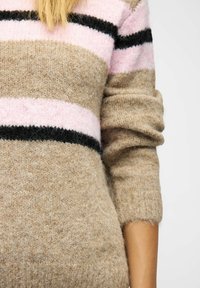 Kootud džemper, mis on valmistatud tekstuursetest beežidest kangast, millel on roosa ja must horisontaalne riba, omades lõdvat istuvust ja keeratud ääri.