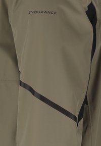 Beigenvärinen kangas, jossa musta vinoraita ja sana "ENDURANCE" painettuna lähellä yläosaa keskellä.