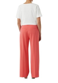 Biała krótka koszulka z podwiniętymi rękawami zestawiona z koralowymi spodniami o szerokich nogawkach z dwoma tylnymi kieszeniami i gładką teksturą.