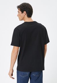 Camiseta de algodón negra con mangas cortas, cuello redondo y un ajuste relajado. Presenta una textura suave y un dobladillo recto.