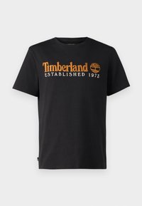 Černé bavlněné tričko s oranžovou vyšívanou nášivkou "Timberland", textem "ESTABLISHED 1973" a grafikou stromu. Klasický design s kulatým výstřihem.