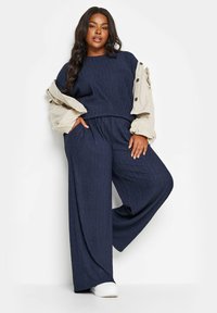 Marinblå texturerad tvådelad outfit med en löst sittande topp och vida byxor, lagd med en ljusbeige oversized jacka och vita sneakers.