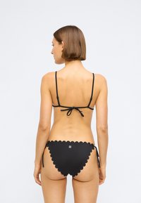 Μαύρο μπικίνι σετ με οδοντωτές άκρες, ρυθμιζόμενες τιράντες με κορδόνια και κλασικό τρίγωνο σχήμα. Λεία υφή και ελάχιστη σήμανση στο πίσω μέρος.
