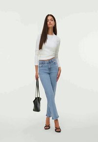 Λευκή μπλούζα μακρυμάνικη, ανοιχτό μπλε τζιν ψηλόμεσο, μαύρες σανδάλες με λουριά και μικρή μαύρη τσάντα, με λείο ύφασμα και εφαρμοστή σχεδίαση.