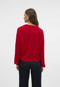 Maglione rosso lavorato a maglia con maniche lunghe e morbide e scollatura rotonda. La parte posteriore ha una vestibilità rilassata, abbinata a pantaloni in denim blu scuro.