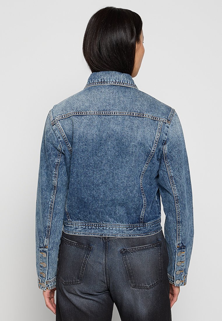 Chaqueta de denim en azul claro con un diseño corto, que presenta un cuello clásico y puños de botón. Textura suave con detalles descoloridos.