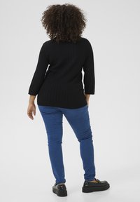 Top de punto negro con acanalado y mangas tres cuartos, combinado con jeans ajustados azules y zapatos de plataforma negros. Fondo neutro.