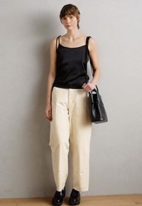 Black satin sleeveless top, beige wide-leg trousers, black handbag, and chunky black footwear. Model stands against a neutral background.