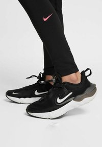 Baskets de sport noires avec accents blancs, tige en mesh, semelle arrondie, système de laçage ajustable et logo Nike bien visible.