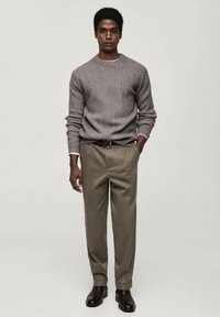 Gray ribbed sweater with a round neckline, paired with loose beige trousers and dark brown leather boots, worn by a man standing straight.