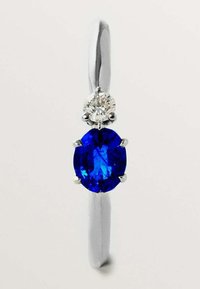 Anillo de plata con un ópalo azul en forma ovalada, acentuado por un pequeño diamante redondo en la parte superior. Superficie pulida y lisa, diseño elegante y minimalista.