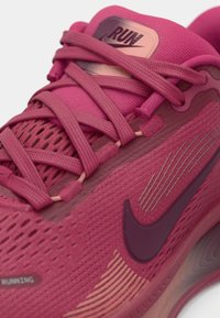 Rožinė bėgimo batelis su tekstūruotu tinklu, sustiprinta raištelių sistema ir tono Nike logotipu. Įrengtas gradientinis padas ir matoma amortizacija.