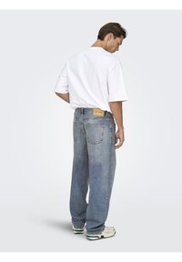 Jean en denim bleu large à taille haute, avec des poches arrière appliquées et une étiquette en cuir fauve. Associé à un t-shirt blanc uni à manches courtes.