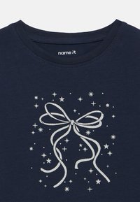 T-shirt in cotone blu navy con un design a fiocco glitterato argento circondato da piccole stelle e puntini. Collo a giro e maniche corte.