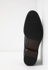 Scarpa in pelle nera con punta a mandorla, dettagli di cucitura, finitura liscia e tacco marrone a contrasto. Suola in gomma texture. Taglia 42.