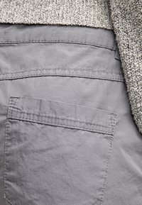 Pantalones de tela gris con un bolsillo trasero visible y un suéter beige texturizado en contraste. Textura suave, costuras estructuradas y minimalismo en los detalles.