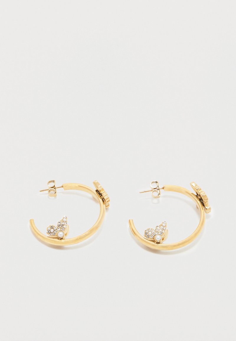 Orecchini a cerchio dorati con piccole decorazioni a forma di foglia adornate con perle e cristalli vicino alla base, esposti su uno sfondo bianco.