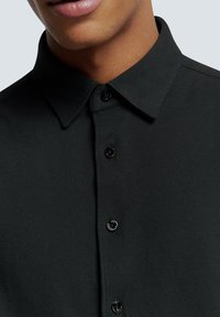 Zwarte shirt met een button-down kraag, textuursstof en zwarte knopen, met een strakke afwerking en geen zichtbare patronen of accenten.