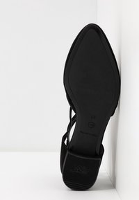 Semelle d'une chaussure habillée noire à bout pointu avec talon antidérapant, taille 37, reposant debout contre un mur blanc.