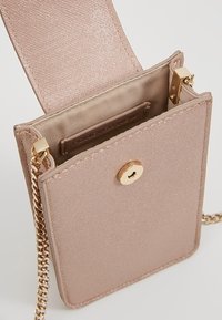 Różowo-złota torebka na ramię z fakturowaną powierzchnią, złotymi okuciami, zapięciem na zatrzask i łańcuszkowym paskiem. Wnętrze wyłożone miękką beżową tkaniną.