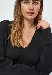 Schwarzer V-Ausschnitt-Pullover mit lockerer Passform, gerippten Bündchen und weicher Textur. Der Stoff fällt sanft und betont den Halsausschnitt und die Ärmel.