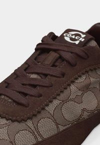 Baskets Coach marron avec motif monogramme en tissu, garniture en daim et lacets marron, avec une étiquette de languette de marque.